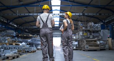 Factory workers walking through large production hall and having conversation.