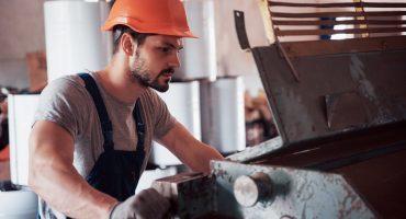 Portrait of a young worker in a hard hat at a large waste recycling factory. The engineer monitors the work of machines and other equipment
