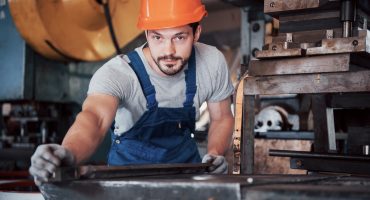 Portrait of a young worker in a hard hat at a large waste recycling factory. The engineer monitors the work of machines and other equipment
