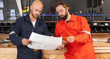 Two builders in work clothes thoughtfully looking on sketch with